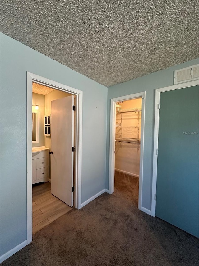 unfurnished bedroom with ensuite bath, a textured ceiling, a walk in closet, a closet, and carpet