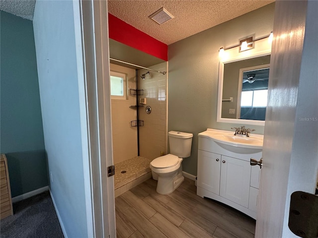 bathroom with a textured ceiling, vanity, toilet, and tiled shower