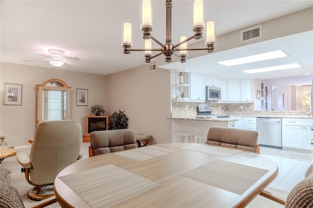 dining room featuring ceiling fan with notable chandelier, light tile patterned flooring, sink, and a skylight