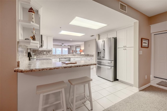 kitchen with white cabinetry, stainless steel appliances, kitchen peninsula, a breakfast bar area, and light tile patterned floors