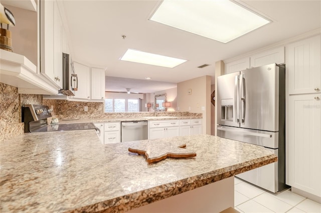 kitchen with kitchen peninsula, appliances with stainless steel finishes, decorative backsplash, light tile patterned floors, and white cabinetry