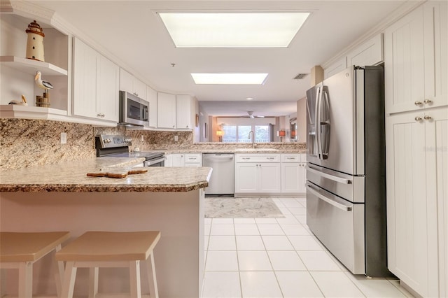 kitchen featuring white cabinetry, stainless steel appliances, kitchen peninsula, a kitchen bar, and light tile patterned floors