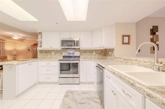 kitchen with kitchen peninsula, appliances with stainless steel finishes, sink, white cabinetry, and light tile patterned flooring