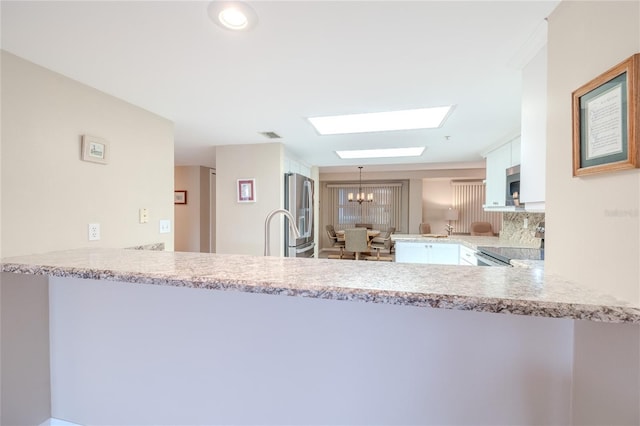 kitchen featuring a notable chandelier, white cabinets, decorative light fixtures, kitchen peninsula, and stainless steel appliances