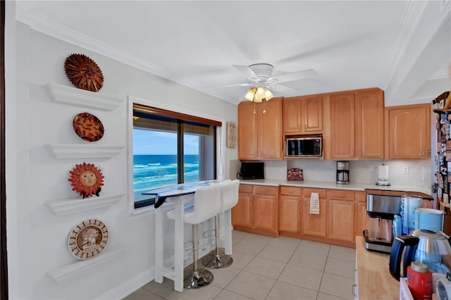 kitchen with ceiling fan, stainless steel microwave, light tile patterned floors, and ornamental molding