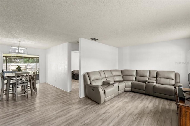 living room with light wood-type flooring, a textured ceiling, and an inviting chandelier