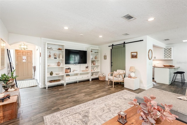 living room featuring a barn door, dark hardwood / wood-style flooring, and a textured ceiling