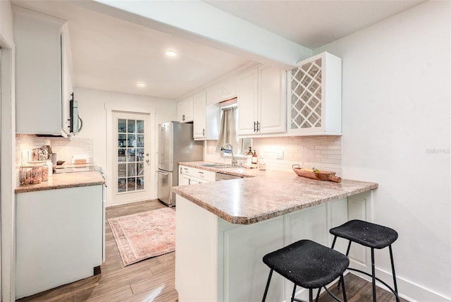 kitchen with white cabinets, sink, light hardwood / wood-style floors, a kitchen bar, and stainless steel refrigerator