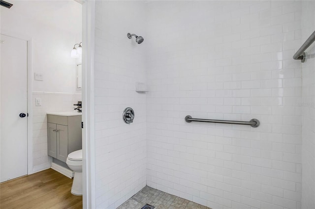 bathroom featuring tiled shower, hardwood / wood-style floors, vanity, and toilet