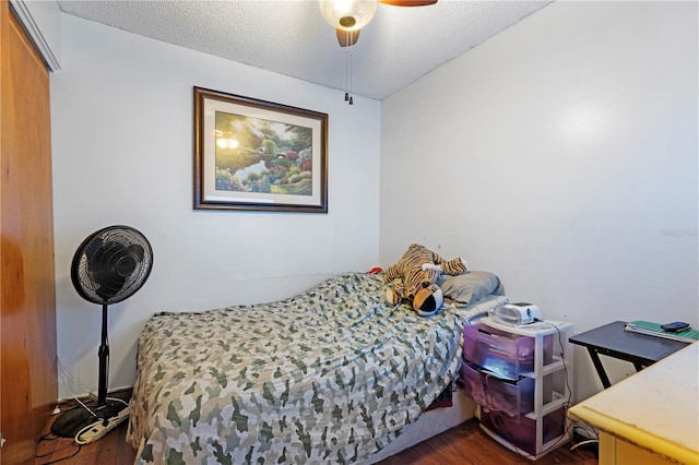 bedroom with a textured ceiling, ceiling fan, and dark wood-type flooring