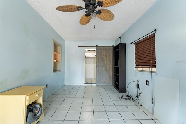 tiled empty room featuring a barn door, ceiling fan, and a textured ceiling