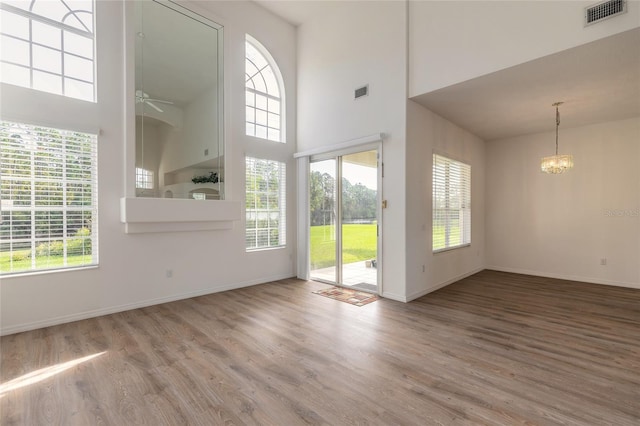 interior space with wood-type flooring, ceiling fan with notable chandelier, a wealth of natural light, and a high ceiling