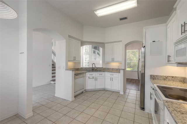 kitchen featuring light stone countertops, white appliances, sink, light tile patterned floors, and white cabinetry