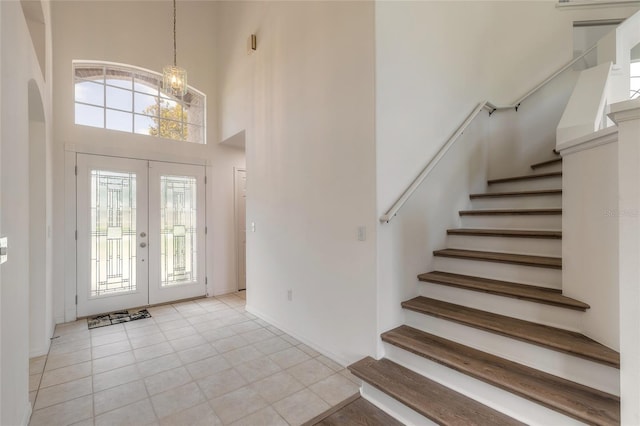 tiled entrance foyer with an inviting chandelier, a towering ceiling, and french doors