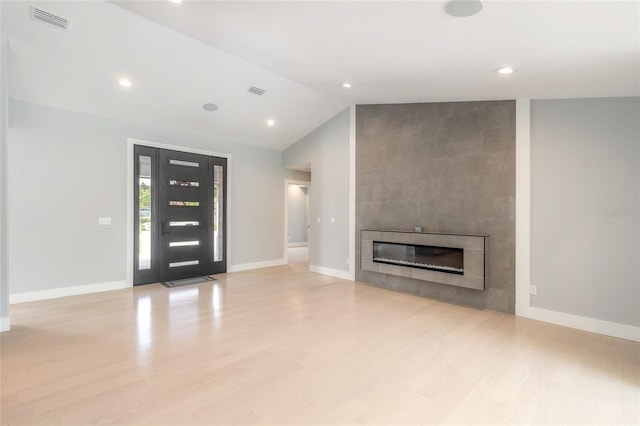 unfurnished living room with a tiled fireplace, light hardwood / wood-style flooring, and vaulted ceiling