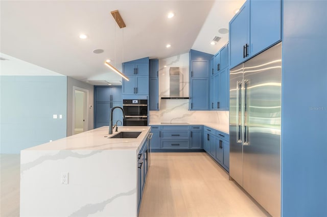 kitchen featuring light wood-type flooring, stainless steel built in refrigerator, blue cabinetry, a center island with sink, and hanging light fixtures