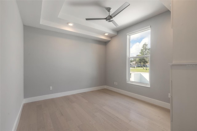 unfurnished room with a raised ceiling, ceiling fan, and light hardwood / wood-style floors