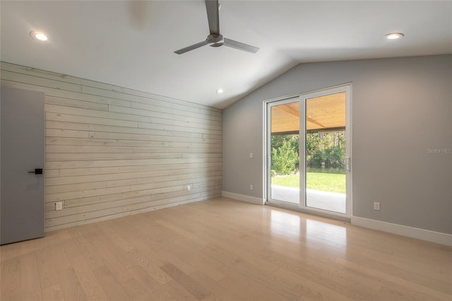 empty room featuring ceiling fan, wooden walls, vaulted ceiling, and light wood-type flooring