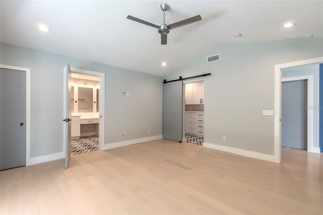 unfurnished bedroom featuring lofted ceiling, ensuite bath, light hardwood / wood-style flooring, ceiling fan, and a barn door