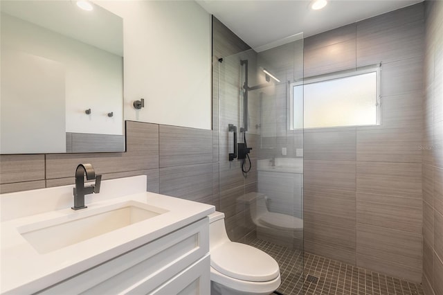 bathroom with vanity, toilet, tiled shower, and tile walls