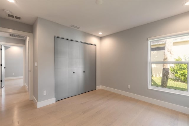 unfurnished bedroom featuring a closet, light wood-type flooring, and multiple windows