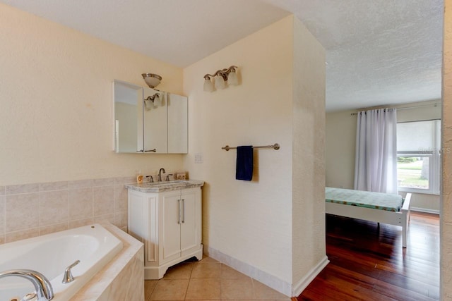 bathroom with tiled tub, vanity, tile patterned floors, and a textured ceiling