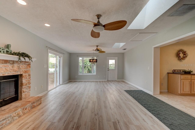 living room featuring a stone fireplace, a skylight, a textured ceiling, and light wood-type flooring