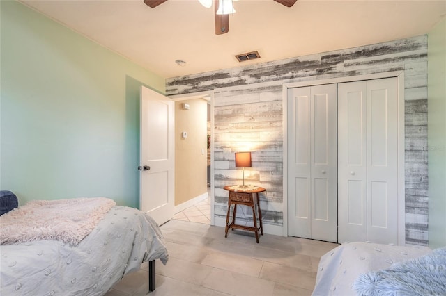 tiled bedroom featuring ceiling fan, wooden walls, and a closet