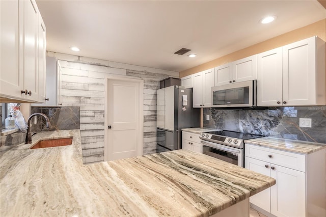 kitchen featuring kitchen peninsula, appliances with stainless steel finishes, light stone counters, sink, and white cabinets