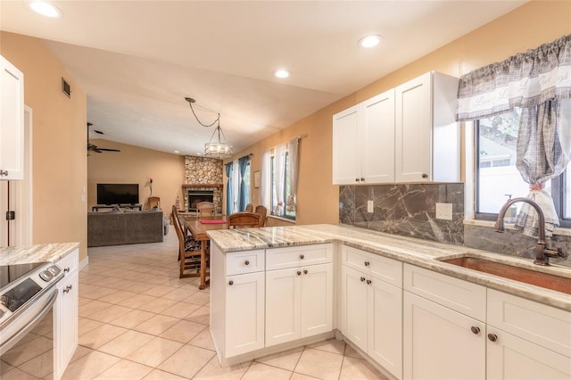 kitchen with kitchen peninsula, sink, white cabinetry, a stone fireplace, and stainless steel electric range