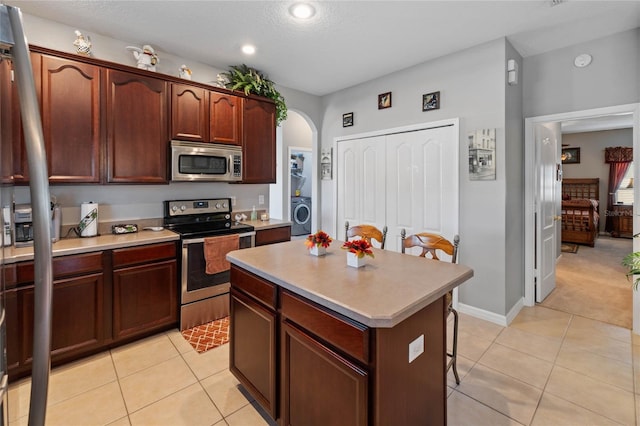 kitchen featuring a kitchen island, washer / dryer, a kitchen bar, light tile patterned floors, and appliances with stainless steel finishes