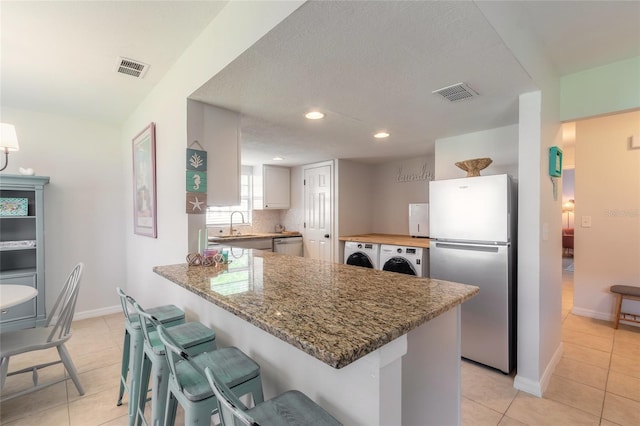 kitchen with light tile patterned floors, appliances with stainless steel finishes, tasteful backsplash, stone countertops, and kitchen peninsula