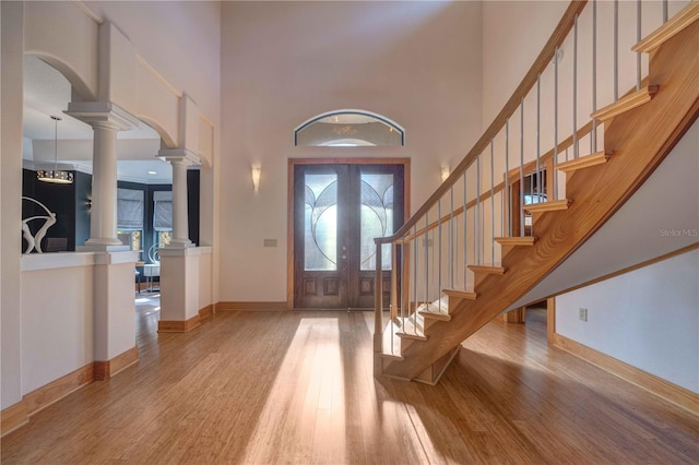 foyer entrance with french doors, a towering ceiling, light hardwood / wood-style flooring, and ornate columns