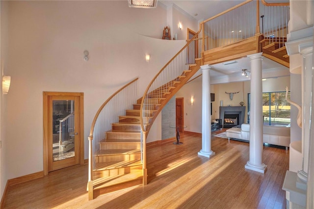 stairway featuring hardwood / wood-style flooring, ornate columns, ornamental molding, and a high ceiling