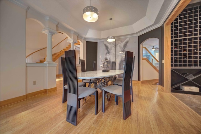 dining area featuring decorative columns, ceiling fan, a tray ceiling, and light hardwood / wood-style floors