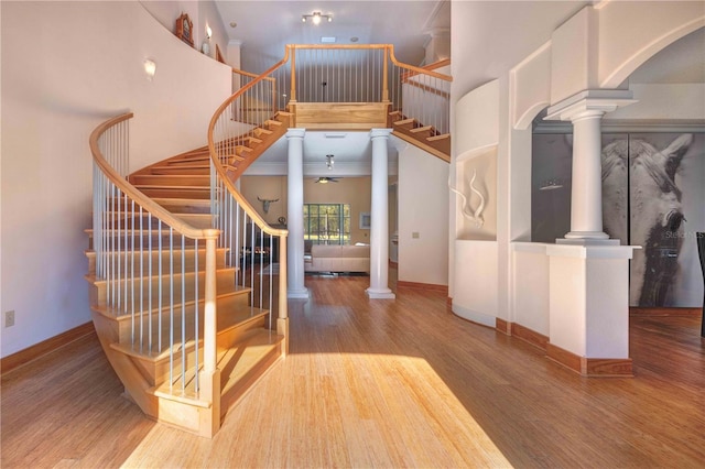 staircase featuring wood-type flooring, decorative columns, ceiling fan, and a high ceiling