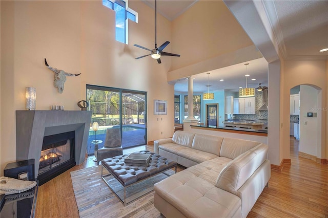 living room with ceiling fan, ornate columns, a high ceiling, and light hardwood / wood-style flooring