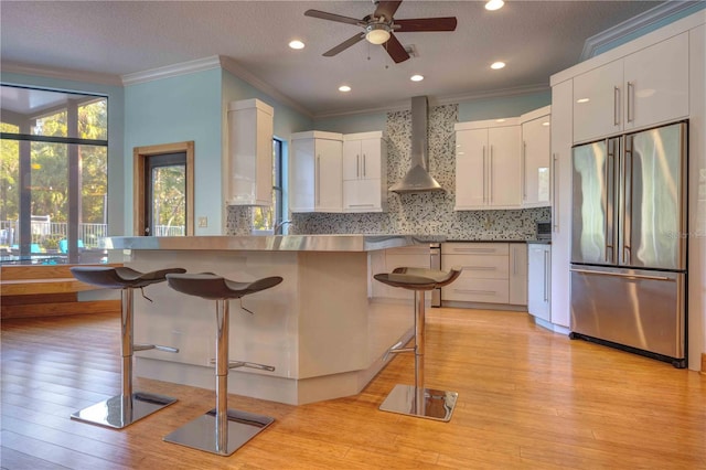 kitchen featuring a kitchen breakfast bar, white cabinets, high end fridge, and wall chimney exhaust hood