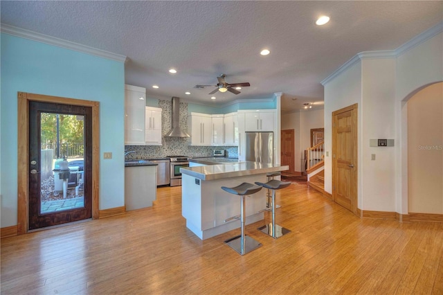 kitchen with white cabinets, light hardwood / wood-style floors, stainless steel appliances, and wall chimney exhaust hood