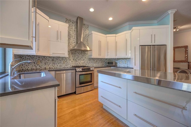 kitchen with appliances with stainless steel finishes, white cabinetry, wall chimney exhaust hood, and sink