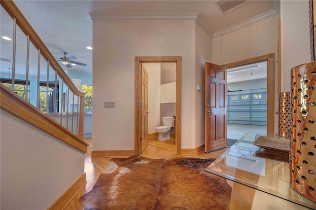 hallway with ornamental molding, a textured ceiling, and light hardwood / wood-style flooring