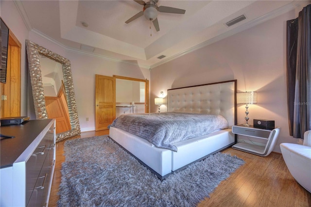 bedroom with wood-type flooring, a tray ceiling, ceiling fan, and crown molding