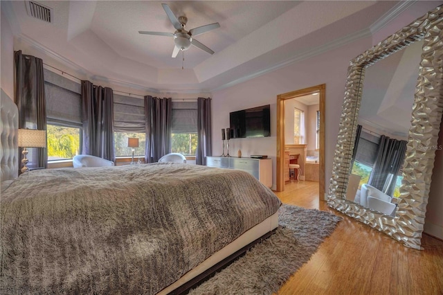 bedroom with ensuite bath, ceiling fan, a raised ceiling, light wood-type flooring, and ornamental molding