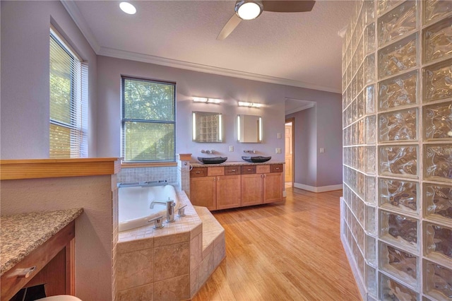 bathroom featuring vanity, crown molding, hardwood / wood-style flooring, a relaxing tiled tub, and a textured ceiling