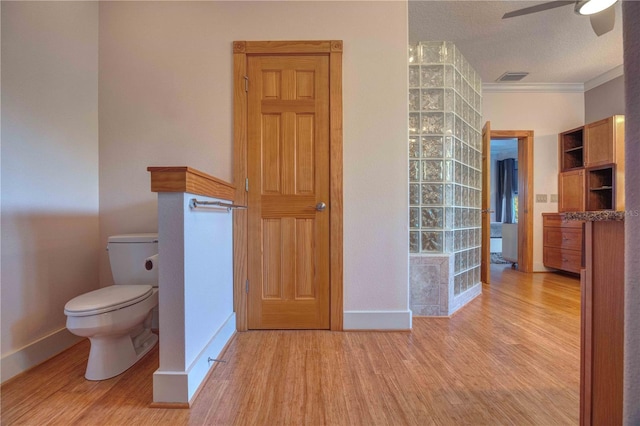 bathroom featuring ceiling fan, crown molding, wood-type flooring, a textured ceiling, and toilet