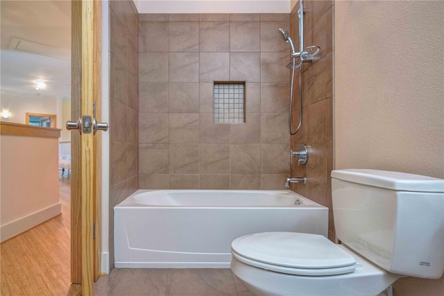 bathroom with hardwood / wood-style floors, toilet, and tiled shower / bath