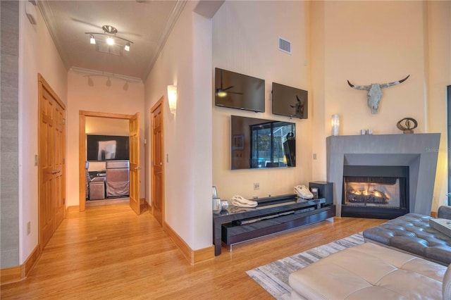 living room featuring a towering ceiling, ornamental molding, and light wood-type flooring