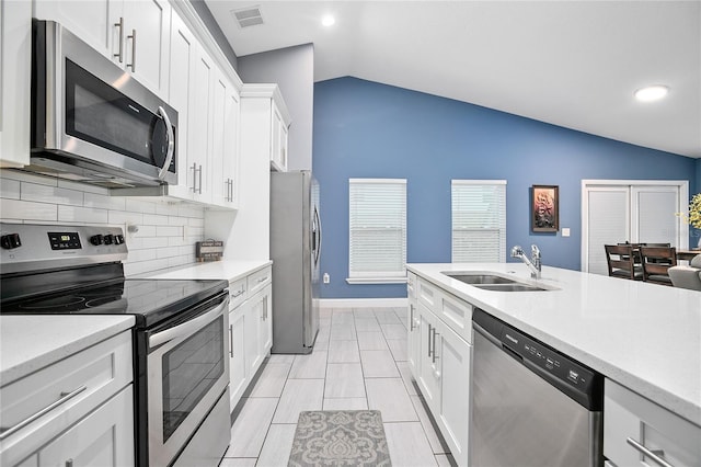 kitchen with appliances with stainless steel finishes, backsplash, sink, white cabinets, and lofted ceiling