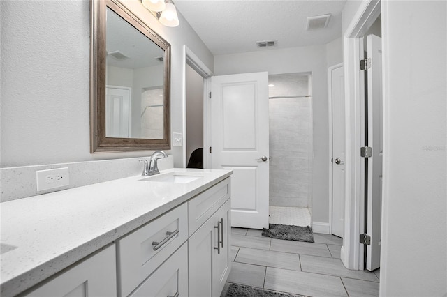 bathroom featuring a textured ceiling, vanity, and tiled shower