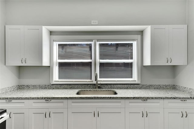 kitchen featuring light stone countertops, sink, and white cabinets